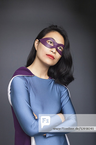 Nachdenklicher weiblicher Superheld mit gekreuzten Armen auf grauem Hintergrund.