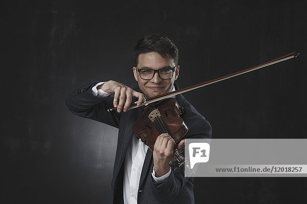 Selbstbewusst lächelnder junger Mann beim Geigenspiel vor schwarzem Hintergrund