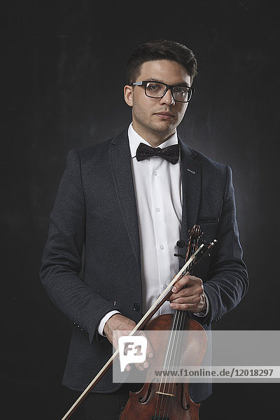Porträt eines selbstbewussten jungen Mannes mit Geige auf schwarzem Hintergrund