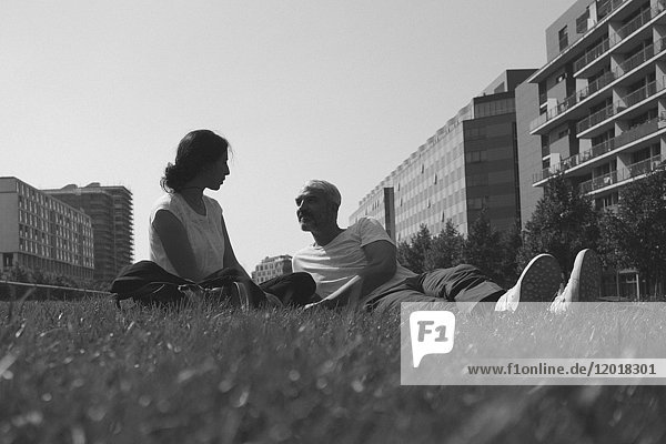 Couple resting on grassy field against clear sky in city