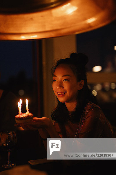 Glückliche Frau hält kleine Geburtstagstorte mit Kerzen in der Dunkelkammer