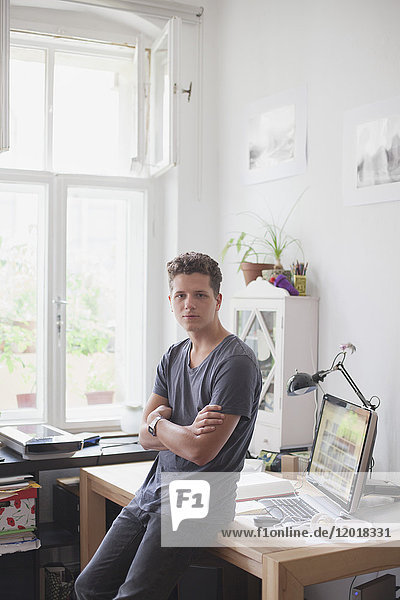 Portrait of handsome man leaning with arms crossed on table at home