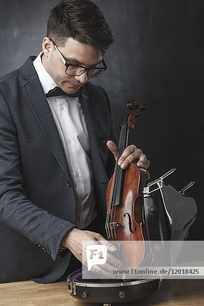 Junger Mann mit Geige im Etui vor schwarzem Hintergrund
