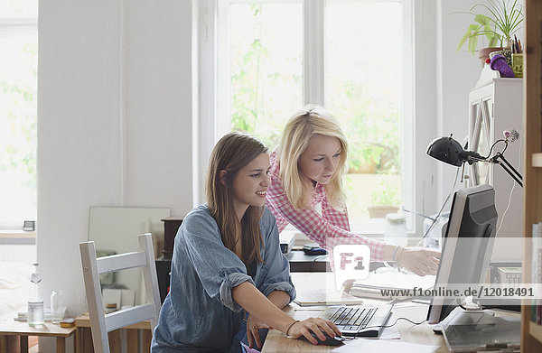 Blond woman pointing at computer monitor to female friend
