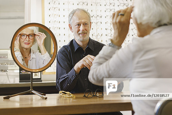 Optikerin unterstützt Seniorin bei der Brillenauswahl im Geschäft