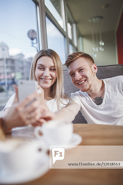 Happy young couple taking selfie with mobile phone while sitting at restaurant