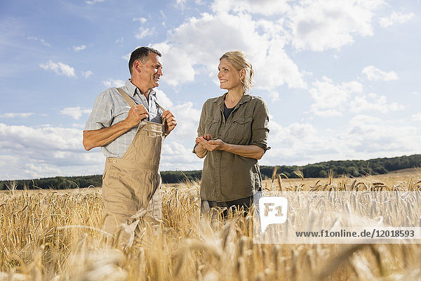 Happy mature couple talking while standing amidst crops at farm against sky