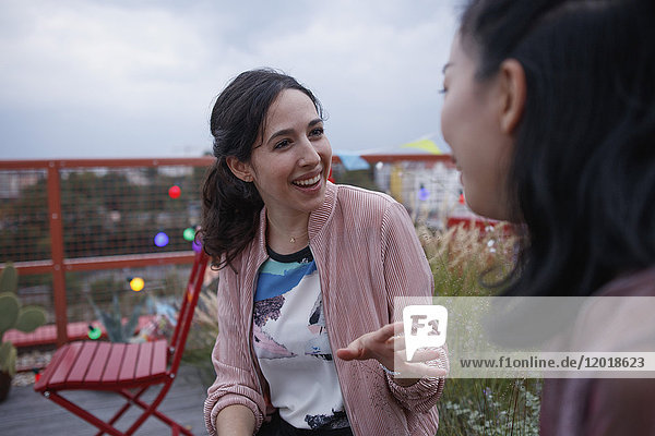 Happy woman talking to female friend while sitting on patio