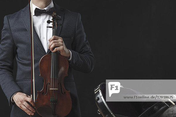 Mittelteil des Mannes  der die Geige hält  während er vor schwarzem Hintergrund steht.