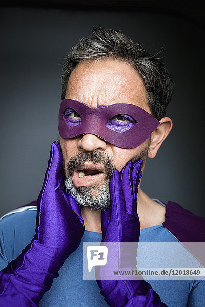 Porträt des Superhelden mit Händen auf den Wangen vor grauem Hintergrund