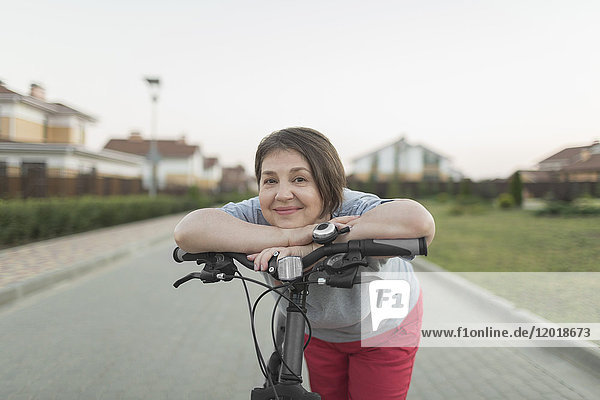 Porträt einer älteren Frau  die sich auf der Straße über den Fahrradgriff lehnt.