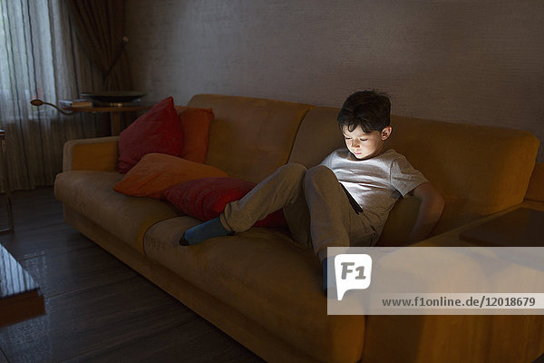 Full length of boy using digital tablet while sitting on sofa at home