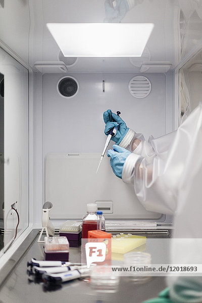 Abgeschnittenes Bild eines Wissenschaftlers  der die Pipette über eine Maschine im Labor hält.