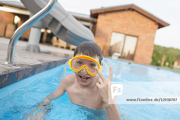 Porträt eines Jungen ohne Hemd mit Friedenszeichen beim Schwimmen im Pool