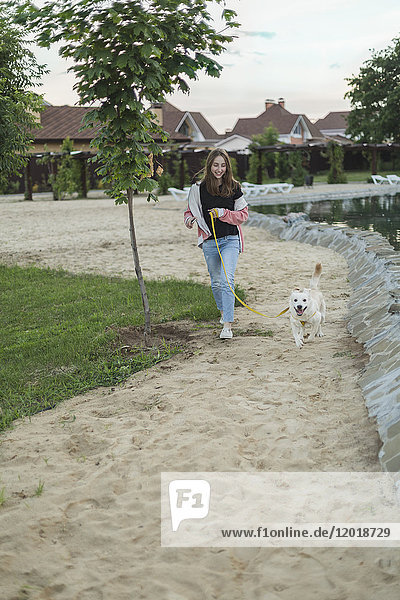 Lächelndes Teenagermädchen läuft mit Hund auf Sand