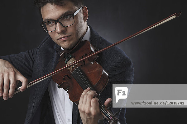 Gutaussehender Mann in Formalen beim Geigenspiel vor schwarzem Hintergrund