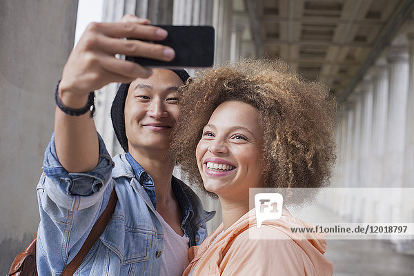 Lächelnder junger Mann nimmt Selfie mit weiblicher Freundin im Flur