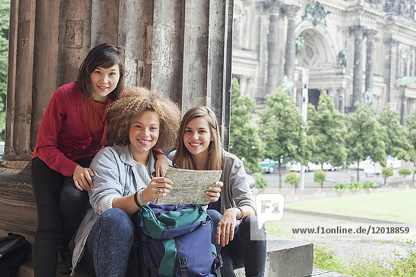 Portrait of young female tourists sitting with map at Altes Museum against Berlin Cathedral  Germany