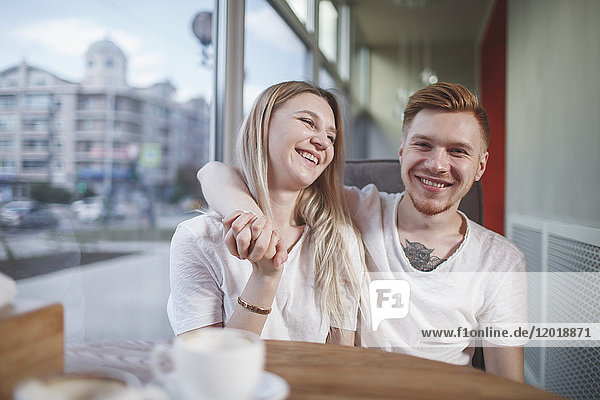 Porträt eines lächelnden Mannes  der mit seiner Freundin im Restaurant sitzt.