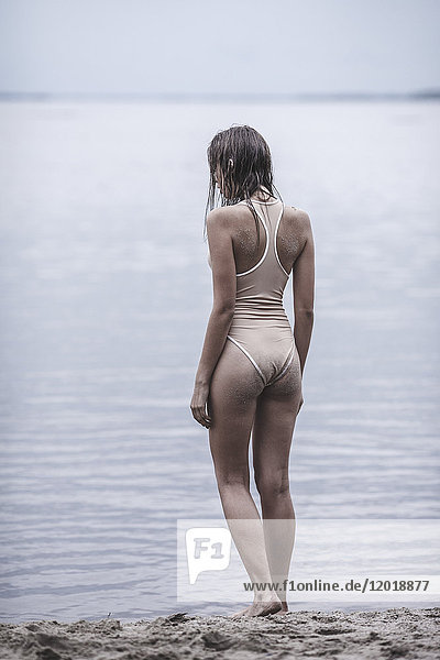 Rear view of woman wearing one piece swimsuit standing at lakeshore