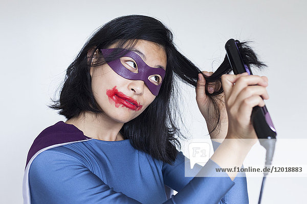 Weiblicher Superheld mit verschmiertem Lippenstift  der die Haare vor grauem Hintergrund glättet.