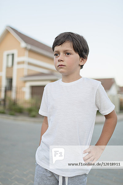 Thoughtful boy standing with hand on hip in town against clear sky
