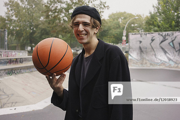 Fröhlicher junger Mann beim Basketballspielen im Park