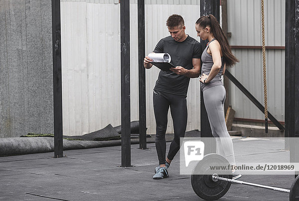 Male coach instructing female athlete over clipboard during crossfit training