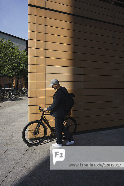 Full length of businessman with bicycle standing by wall on sunny day
