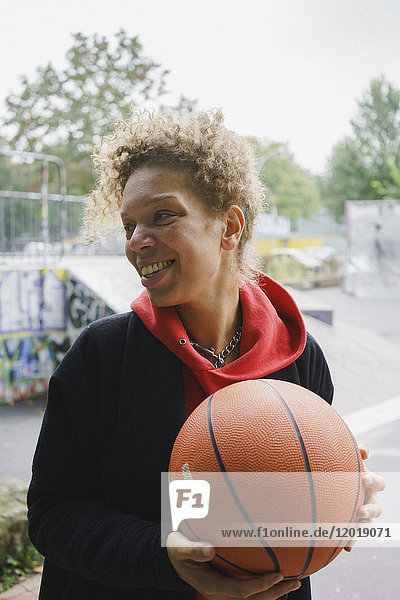 Lächelnde erwachsene Frau hält Basketball während sie im Park steht.