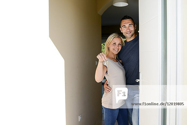 Glückliches junges Paar an der Eingangstür des neuen Hauses  das stolz seinen Hausschlüssel zeigt.