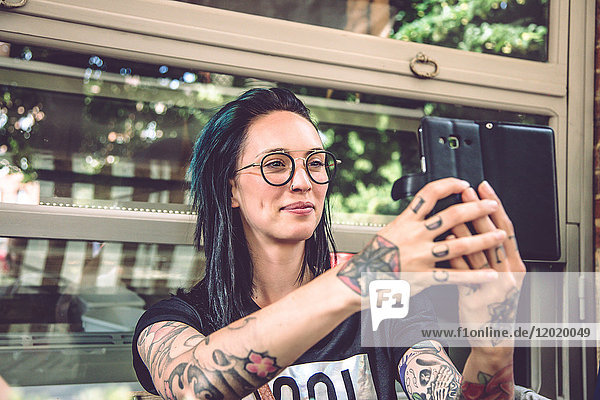 Porträt einer jungen Frau  die auf einer Restaurantterrasse sitzt und ein Selfie macht