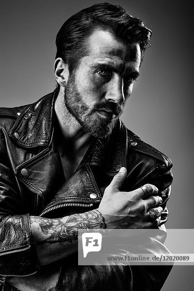 Portrait of a young tattooed man in profile  wearing a leather jacket Perfecto under gray background