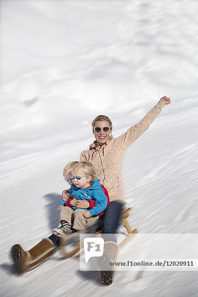 Portrait of smiling woman sitting with her childs on sled in snow  Crans-Montana  Swiss Alps  Switzerland.