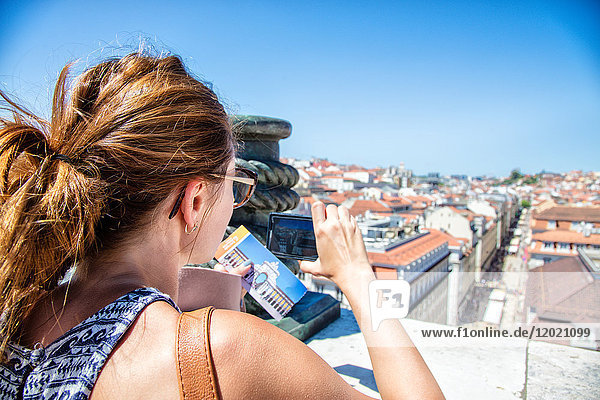 Porträt einer jungen Frau von hinten  die ein Foto mit seinem Smartphone auf der Höhe eines Batiements am Commerce Square  Lissabon  Portugal  macht