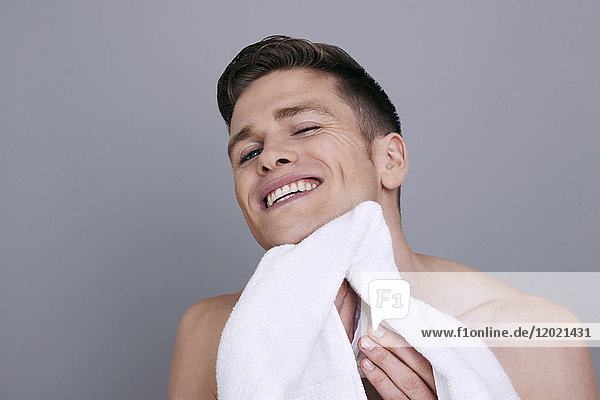 Oben-ohne-Mann  der sein Kinn und seinen Hals nach der Rasur mit einem Handtuch abtrocknet  lächelnd