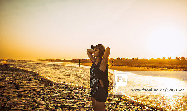 Junge Frau Hände hinter dem Kopf  halten das Meer am Strand Praia do Barril in einem Sonnenuntergang  deTavira Stadt  Region Algarve  Portugal