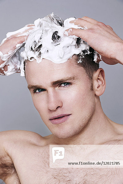 Oben-ohne-Mann  mit Shampoo in den Haaren  schaut in die Kamera  ernst  wäscht sich die Haare  mit Schaum auf dem Kopf