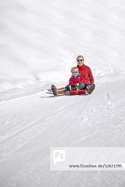 Porträt einer lächelnden Frau  die mit ihren Kindern auf einem Schlitten im Schnee sitzt  Crans-Montana  Schweizer Alpen  Schweiz.