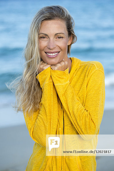 Porträt einer lächelnden jungen blonden Frau in Gelb  die im Meer schwimmt.