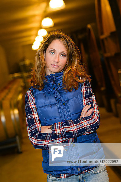 Fröhliche junge Winzerin posiert in ihrem Keller mit einem Weinfass im Hintergrund - Cepage Grenache  Chateauneuf du Pape  cotes du Rhone  Frankreich