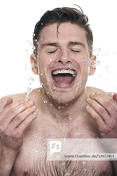 Oben-ohne-Mann  Wasser auf sein Gesicht spritzend  Augen geschlossen  Mund geöffnet  lächelnd