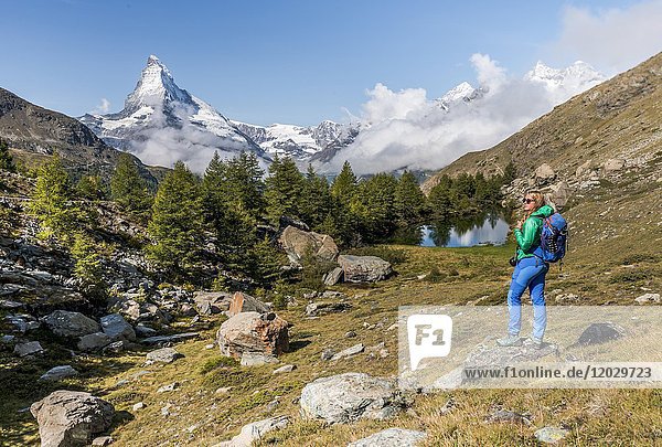 Hiker stands on rocks and looks into the distance  behind Grindijsee and snow-covered Matterhorn  Valais  Switzerland  Europe
