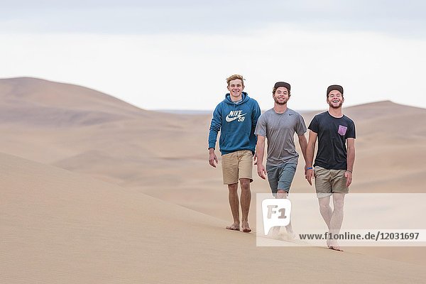 Drei junge Männer laufen über eine Sanddüne  Namib-Wüste  Namibia  Afrika