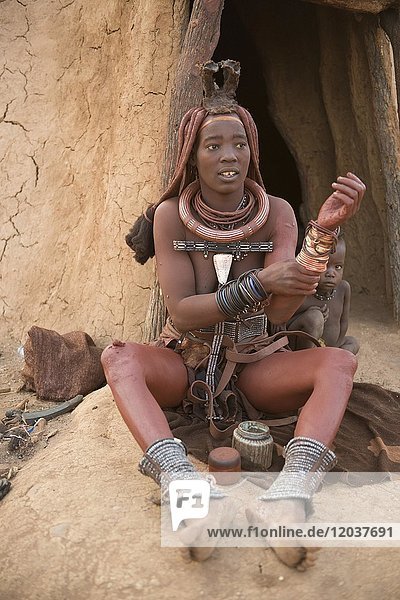 Himbafrau mit Kind vor der Hütte  reibt sich mit Okra ein  Butterfett mit Ockerfarbe  Kaokoveld  Namibia  Afrika