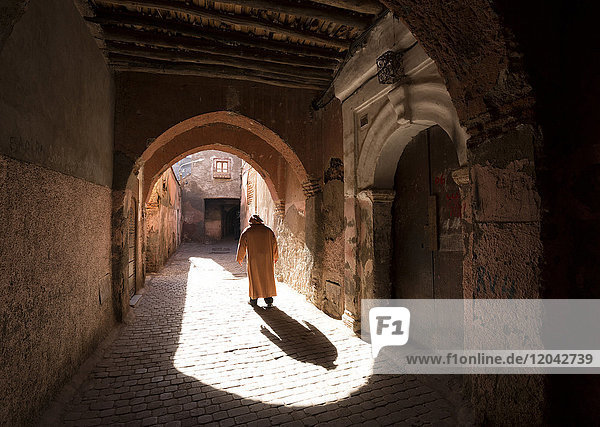 Local man dressed in traditional djellaba walking through archway in a street in the Kasbah Marrakech Morocco North Africa Africa