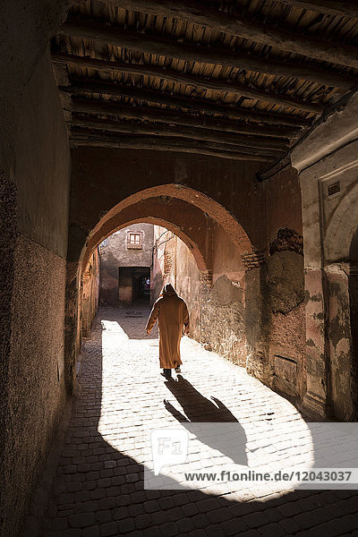 Local man dressed in traditional djellaba walking through archway in a street in the Kasbah Marrakech Morocco North Africa Africa