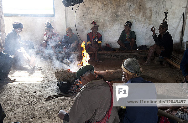 Naga men sitting chatting around the central fire in their village murung (village hall)  Hongphui village  Nagaland  India  Asia