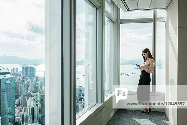 Business woman in skyscraper office window using smartphone