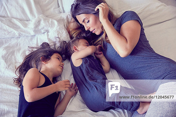 Mother and two young children  lying on bed